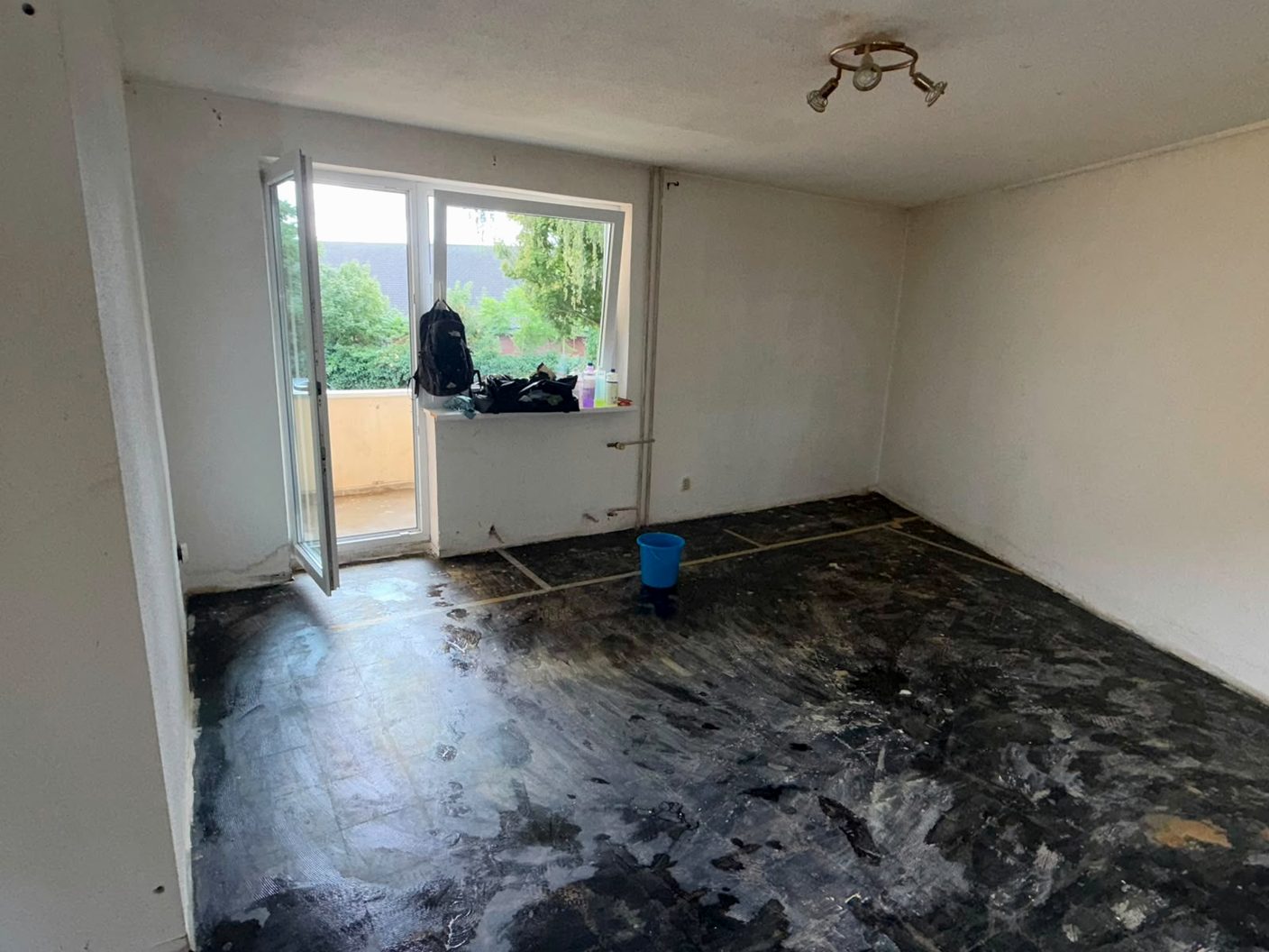 Leergeräumter Wohnraum nach der Haushaltsauflösung, offene Balkontür, Arbeitsrucksack auf der Fensterbank